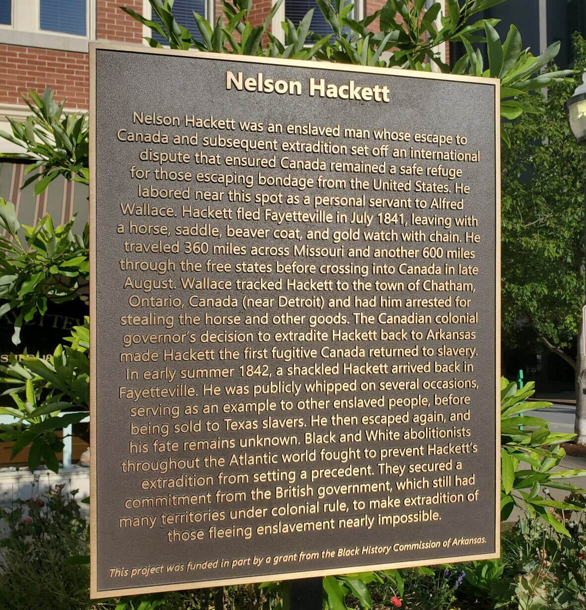 Photo of Marker Of Nelson Hackett. Marker text: Nelson Hackett. Nelson Hackett was an enslaved man whose escape to Canada and subsequent extradition set off an international dispute that ensured Canada remained a safe refuge for those escaping bondage from the United States. He labored near this spot as a personal servant to Alfred Wallace. Hackett fled Fayetteville in July 1841, leaving with a horse, saddle, beaver coat, and gold watch with chain. He traveled 360 miles across Missouri and another 600 miles through the free states before crossing into Canada in late August. Wallace tracked Hackett to the town of Chatham, Ontario, Canada (near Detroit) and had him arrested for stealing the horse and other goods. The Canadian colonial governor's decision to extradite Hackett back to Arkansas made Hackett the first fugitive Canada returned to slavery. In early summer 1842, a shackled Hackett arrived back in Fayetteville. He was publicly whipped on several occasions, serving as an example to other enslaved people, before being sold to Texas slavers. He then escaped again, and his fate remains unknown. Black and White abolitionists throughout the Atlantic world fought to prevent Hackett's extradition from setting a precedent. They secured a commitment from the British government, which still had many territories under colonial rule, to make extradition of those fleeing slavery nearly impossible. This project was funded in part by a grant from the Black History Commission of Arkansas.